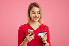 La bella donna felice tiene lo Smart Phone e la carta di credito, effettua il pagamento online, paga l'acquisto in negozio online Fotografia Stock Libera da Diritti La bella donna felice tiene lo Smart Phone e la carta di credito, effettua il pagamento online, paga l'acquisto in negozio online Fotografia Stock Libera da Diritti