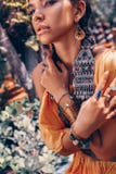 La bella giovane donna alla moda con compone ed accessori alla moda di boho che posano sul fondo tropicale naturale fotografia stock libera da diritti La bella giovane donna alla moda con compone ed accessori alla moda di boho che posano sul fondo tropicale naturale fotografia stock libera da diritti