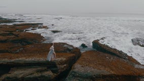 La bella giovane femmina in un vestito sexy lungo posa sulle rocce sulla spiaggia dell'oceano su Bali sul tramonto, il video 4K d stock footage La bella giovane femmina in un vestito sexy lungo posa sulle rocce sulla spiaggia dell'oceano su Bali sul tramonto, il video 4K d stock footage