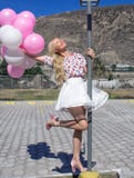 La belle femme, blonde se tient sur un courrier de lampe et tient beaucoup de ballons photo stock La belle femme, blonde se tient sur un courrier de lampe et tient beaucoup de ballons photo stock