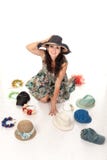 La belle femme choisit des chapeaux Se repose sur le plancher, essayant sur le couvre-chef Beaucoup de différents chapeaux, capot photographie stock La belle femme choisit des chapeaux Se repose sur le plancher, essayant sur le couvre-chef Beaucoup de différents chapeaux, capot photographie stock