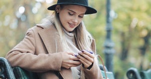La belle femme dans le manteau utilisant le smartphone détend sur le banc en parc d'automne Technologie dehors image libre de droits La belle femme dans le manteau utilisant le smartphone détend sur le banc en parc d'automne Technologie dehors image libre de droits
