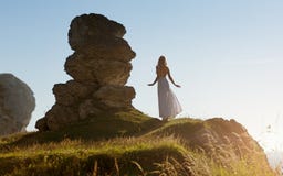 La belle femme mince dans la longue robe blanche se tient à côté d'une formation de roche étrange en Irlande image stock La belle femme mince dans la longue robe blanche se tient à côté d'une formation de roche étrange en Irlande image stock
