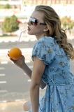 La belle fille boit du jus par une paille d'une orange images stock La belle fille boit du jus par une paille d'une orange images stock