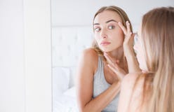 La belle jeune femme, fille touche son visage tout en regardant le miroir Problème sur sa peau photographie stock libre de droits La belle jeune femme, fille touche son visage tout en regardant le miroir Problème sur sa peau photographie stock libre de droits