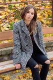 La belle jeune fille avec les yeux tristes de grand automne dans un manteau et les jeans noirs déchirés se reposant sur un banc e images libres de droits La belle jeune fille avec les yeux tristes de grand automne dans un manteau et les jeans noirs déchirés se reposant sur un banc e images libres de droits