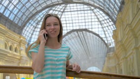La chica joven está hablando en el teléfono móvil en alameda de compras metrajes La chica joven está hablando en el teléfono móvil en alameda de compras metrajes