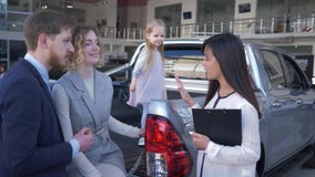 La compra del coche familiar, encargado de la mujer profesional informa a pares jovenes de los clientes con la muchacha del niño almacen de metraje de vídeo La compra del coche familiar, encargado de la mujer profesional informa a pares jovenes de los clientes con la muchacha del niño almacen de metraje de vídeo