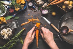 La donna femminile passa le carote della sbucciatura sul tavolo da cucina di legno scuro con le verdure che cucinano gli ingredie La donna femminile passa le carote della sbucciatura sul tavolo da cucina di legno scuro con le verdure che cucinano gli ingredie