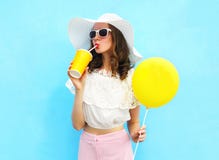 La donna graziosa di modo in cappello di paglia con l'aerostato beve il succo di frutta dalla tazza sopra il blu variopinto fotografia stock libera da diritti La donna graziosa di modo in cappello di paglia con l'aerostato beve il succo di frutta dalla tazza sopra il blu variopinto fotografia stock libera da diritti