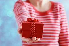 La donna passa la tenuta un regalo o della scatola attuale con l'arco del nastro rosso per il giorno di biglietti di S. Valentino fotografia stock La donna passa la tenuta un regalo o della scatola attuale con l'arco del nastro rosso per il giorno di biglietti di S. Valentino fotografia stock