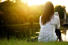 la donna sta sedendosi sul prato inglese Sta utilizzando uno Smart Phone dallo stagno in un parco fotografia stock libera da diritti la donna sta sedendosi sul prato inglese Sta utilizzando uno Smart Phone dallo stagno in un parco fotografia stock libera da diritti