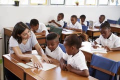 La escuela de ayuda del profesor voluntario embroma en sus escritorios foto de archivo La escuela de ayuda del profesor voluntario embroma en sus escritorios foto de archivo