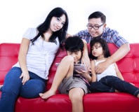 La famiglia felice gode del tempo al sofà rosso - isolato fotografia stock libera da diritti La famiglia felice gode del tempo al sofà rosso - isolato fotografia stock libera da diritti