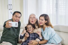 La famiglia sorridente della generazione tre prende il selfie a casa fotografia stock La famiglia sorridente della generazione tre prende il selfie a casa fotografia stock