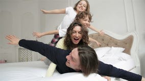 La familia feliz que lleva los pijamas se está divirtiendo en el dormitorio Dos niños de Playfull con el pelo rizado y la pareja metrajes La familia feliz que lleva los pijamas se está divirtiendo en el dormitorio Dos niños de Playfull con el pelo rizado y la pareja metrajes