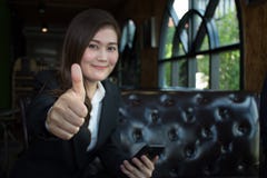 La femme d'affaires de sourire heureuse avec des pouces lèvent le geste regardant l'appareil-photo se reposant sur un sofa photo stock La femme d'affaires de sourire heureuse avec des pouces lèvent le geste regardant l'appareil-photo se reposant sur un sofa photo stock