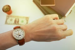 La femme d'affaires regarde la montre sur son poignet, au-dessus d'une table blanche sur laquelle l'argent et les journaux intime photographie stock libre de droits La femme d'affaires regarde la montre sur son poignet, au-dessus d'une table blanche sur laquelle l'argent et les journaux intime photographie stock libre de droits