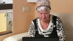 La femme a vieilli travailler sur l'ordinateur portable à la maison sur le divan Elle regarde l'écran et appuie sur fixement la t clips vidéos La femme a vieilli travailler sur l'ordinateur portable à la maison sur le divan Elle regarde l'écran et appuie sur fixement la t clips vidéos
