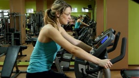 La fille attirante et sportive fait un cycle dans le gymnase de forme physique banque de vidéos La fille attirante et sportive fait un cycle dans le gymnase de forme physique banque de vidéos