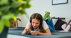 La fille d'adolescent ont l'amusement avec la pose mobile sur le lit écoutant la musique d'un smartphone Images libres de droits La fille d'adolescent ont l'amusement avec la pose mobile sur le lit écoutant la musique d'un smartphone Images libres de droits