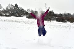 La fille de sourire saute et tombe dans la neige images libres de droits La fille de sourire saute et tombe dans la neige images libres de droits