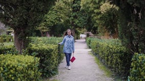 La fille marche en parc le long des buissons verts cisaillés et la mène remettre les feuilles, vue d'ensemble banque de vidéos La fille marche en parc le long des buissons verts cisaillés et la mène remettre les feuilles, vue d'ensemble banque de vidéos