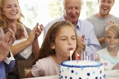 La fille souffle des bougies de gâteau d'anniversaire à la partie de famille image libre de droits La fille souffle des bougies de gâteau d'anniversaire à la partie de famille image libre de droits