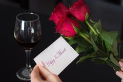 La fille tient une carte de papier avec un message 8 heureux Mars en sa main et verre rouge de rose et de vin sur la table noire photos libres de droits La fille tient une carte de papier avec un message 8 heureux Mars en sa main et verre rouge de rose et de vin sur la table noire photos libres de droits