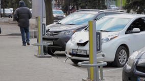 La gente cammina vicino al veicolo elettrico parcheggiato collegato al caricatore da cavo Il hashtag dell'iscrizione annuncia Osc video d archivio La gente cammina vicino al veicolo elettrico parcheggiato collegato al caricatore da cavo Il hashtag dell'iscrizione annuncia Osc video d archivio