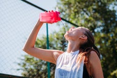 La giovane donna bionda sportiva con la bottiglia sportiva con acqua fresca versa l'acqua se stessa sul campo sportivo immagini stock La giovane donna bionda sportiva con la bottiglia sportiva con acqua fresca versa l'acqua se stessa sul campo sportivo immagini stock