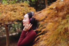 La giovane donna cinese asiatica che ascolta la musica con le cuffie si siede sotto l'albero immagine stock libera da diritti La giovane donna cinese asiatica che ascolta la musica con le cuffie si siede sotto l'albero immagine stock libera da diritti