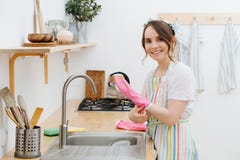 La giovane donna felice in una cucina sta lavando le tazze ed i piatti fotografia stock La giovane donna felice in una cucina sta lavando le tazze ed i piatti fotografia stock