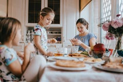 La giovane madre preoccupantesi e le sue due piccole figlie hanno una prima colazione nella cucina leggera con la grande finestra fotografia stock libera da diritti La giovane madre preoccupantesi e le sue due piccole figlie hanno una prima colazione nella cucina leggera con la grande finestra fotografia stock libera da diritti