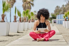 La giovane seduta afroamericana della donna ha attraversato la musica d'ascolto f delle gambe fotografie stock La giovane seduta afroamericana della donna ha attraversato la musica d'ascolto f delle gambe fotografie stock