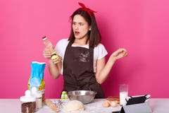 La giovane signora incantante che fa il forno in cucina, usa molti ingredienti e gli utensili per pasta d'impastamento, guarda co fotografie stock libere da diritti La giovane signora incantante che fa il forno in cucina, usa molti ingredienti e gli utensili per pasta d'impastamento, guarda co fotografie stock libere da diritti