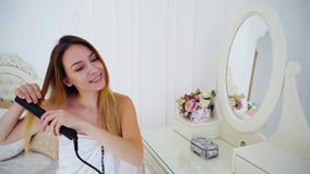 La hembra encantadora alinea el pelo usando los hierros que se encrespan y el pelo hecho, sentándose en silla fotografía de archivo La hembra encantadora alinea el pelo usando los hierros que se encrespan y el pelo hecho, sentándose en silla fotografía de archivo