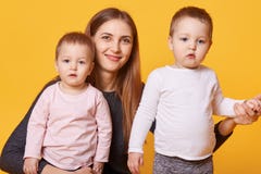 La imagen de la mujer sonriente atractiva con los gemelos de las niñas, daughrer carming lleva ocasional mirada en la cámara, pre foto de archivo La imagen de la mujer sonriente atractiva con los gemelos de las niñas, daughrer carming lleva ocasional mirada en la cámara, pre foto de archivo