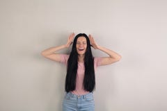 La jeune femme attirante de brune avec de longs cheveux se tient prêt le fond gris tenant ses mains par la tête et criant photographie stock libre de droits La jeune femme attirante de brune avec de longs cheveux se tient prêt le fond gris tenant ses mains par la tête et criant photographie stock libre de droits