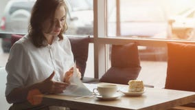 La jeune femme attirante passe le temps gratuit se reposant en cafés, appréciant le café frais et lisant un magazine du ` s de fe photo libre de droits La jeune femme attirante passe le temps gratuit se reposant en cafés, appréciant le café frais et lisant un magazine du ` s de fe photo libre de droits