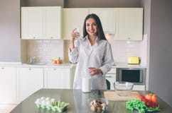 La jeune femme attirante se tient dans la cuisine et la pose Elle regarde l'appareil-photo et le sourire La fille tient la tasse photographie stock libre de droits La jeune femme attirante se tient dans la cuisine et la pose Elle regarde l'appareil-photo et le sourire La fille tient la tasse photographie stock libre de droits