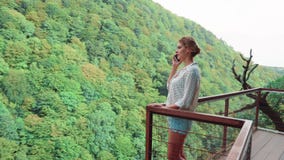 La jeune femme avec les cheveux blonds dans le chemisier à pois blanc léger sur le pont au-dessus du canyon d'Okat et parle par l clips vidéos La jeune femme avec les cheveux blonds dans le chemisier à pois blanc léger sur le pont au-dessus du canyon d'Okat et parle par l clips vidéos