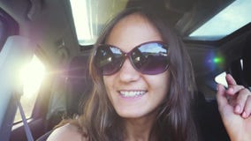 La jeune femme gaie utilise des lunettes de soleil se reposant dans le passager de voiture et chanson de chant dans le mouvement clips vidéos La jeune femme gaie utilise des lunettes de soleil se reposant dans le passager de voiture et chanson de chant dans le mouvement clips vidéos