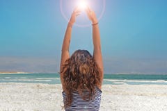 La jeune femme remet attraper l'énergie du soleil la fille aux cheveux longs s'assied sur le rivage de la mer morte en Israël image stock La jeune femme remet attraper l'énergie du soleil la fille aux cheveux longs s'assied sur le rivage de la mer morte en Israël image stock