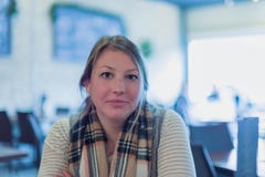 La jeune femme s'asseyant au restaurant, bras a croisé regarder la caméra images stock La jeune femme s'asseyant au restaurant, bras a croisé regarder la caméra images stock