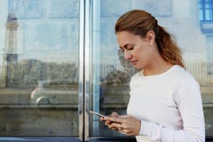 La jeune information attrayante de lecture de femme par l'intermédiaire du réseau au téléphone portable tout en attendant une voi photographie stock La jeune information attrayante de lecture de femme par l'intermédiaire du réseau au téléphone portable tout en attendant une voi photographie stock