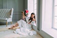 La jeune mariée gaie et jeune tient un bouquet rustique de mariage avec des pivoines sur le fond panoramique de fenêtre Portrait photos libres de droits La jeune mariée gaie et jeune tient un bouquet rustique de mariage avec des pivoines sur le fond panoramique de fenêtre Portrait photos libres de droits