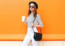 La jolie femme de sourire avec le blanc de port de chapeau noir de mode de tasse de café halète l'embrayage de sac à main au-dess photo libre de droits La jolie femme de sourire avec le blanc de port de chapeau noir de mode de tasse de café halète l'embrayage de sac à main au-dess photo libre de droits
