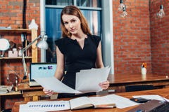 La lettura seria della donna incarta lo studio dei riassunti che stanno allo scrittorio del lavoro in ufficio alla moda fotografia stock La lettura seria della donna incarta lo studio dei riassunti che stanno allo scrittorio del lavoro in ufficio alla moda fotografia stock