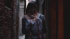 La macchina fotografica segue il turista della donna con lo zaino che cammina lungo la bella vecchia via scura della città a movi stock footage La macchina fotografica segue il turista della donna con lo zaino che cammina lungo la bella vecchia via scura della città a movi stock footage